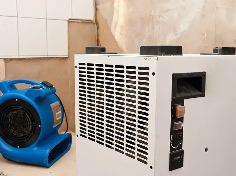 Air mover and dehumidifier beside an opened lower wall