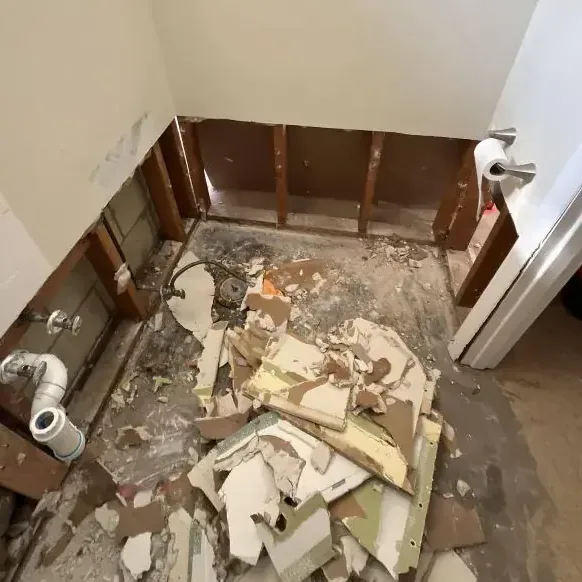 Exposed lower wall framing and broken drywall across a bathroom floor