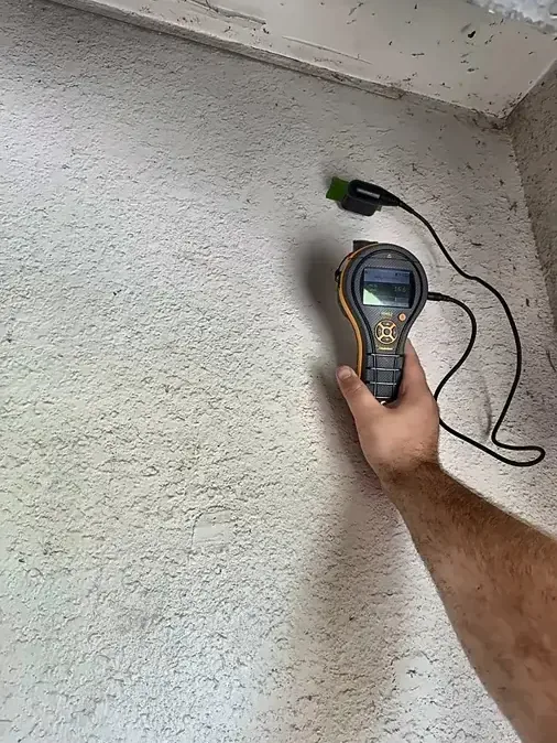 Hand holding a moisture meter against a textured interior wall
