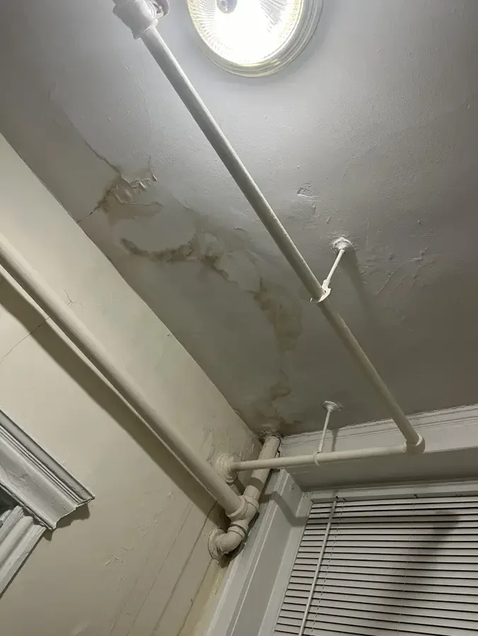 Discolored ceiling beside exposed pipes and a round overhead light