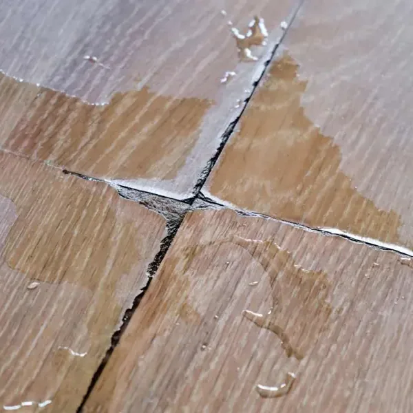 Water droplets collecting on wood flooring beside an open board joint