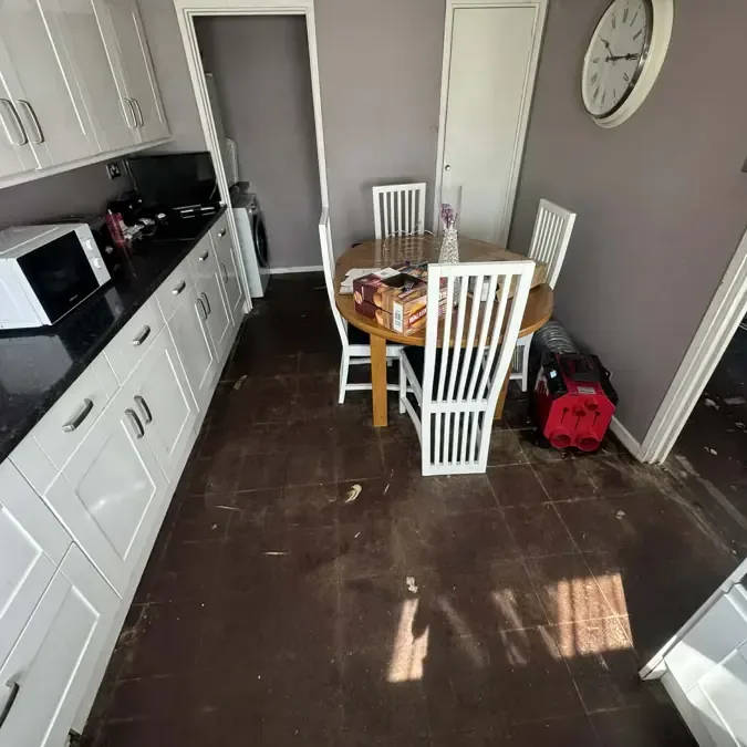 Dark kitchen floor beside white cabinets and a small dining table