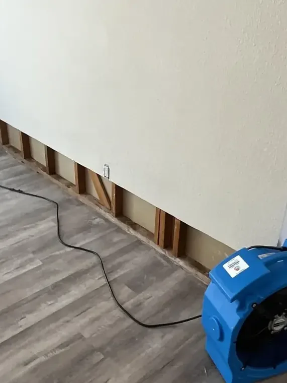 Blue air mover beside exposed studs along an opened lower wall