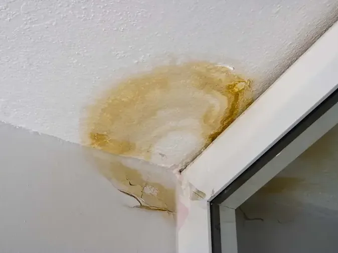 Yellow brown ceiling stain beside the upper corner of a window