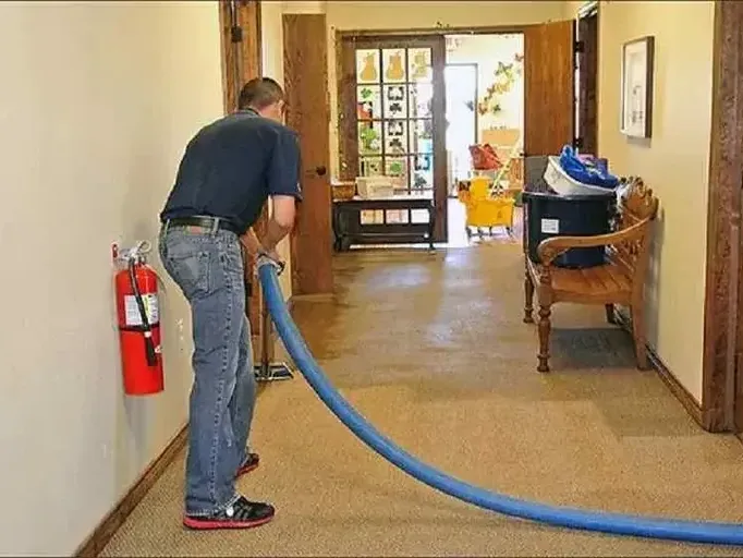 Technician guiding an extraction hose across carpeting in a hallway