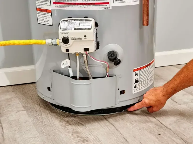 Hand pointing beside a gas water heater base on plank flooring